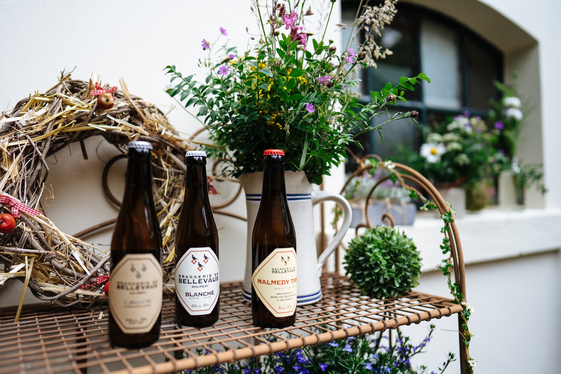 Trois types différents de bière de la brasserie de Bellevaux, sur une étagère dans la cour de la brasserie. Il y a des fleurs sur l'étagère.