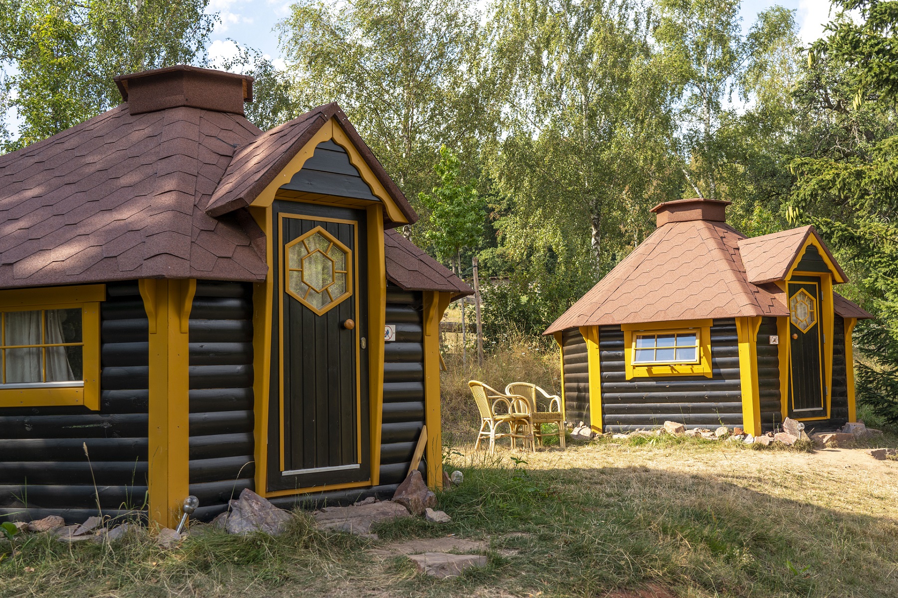 Deux kota finlandais avec des cadres de fenêtres et de portes jaunes. Ils servent d'hébergement pour la nuit au camping.