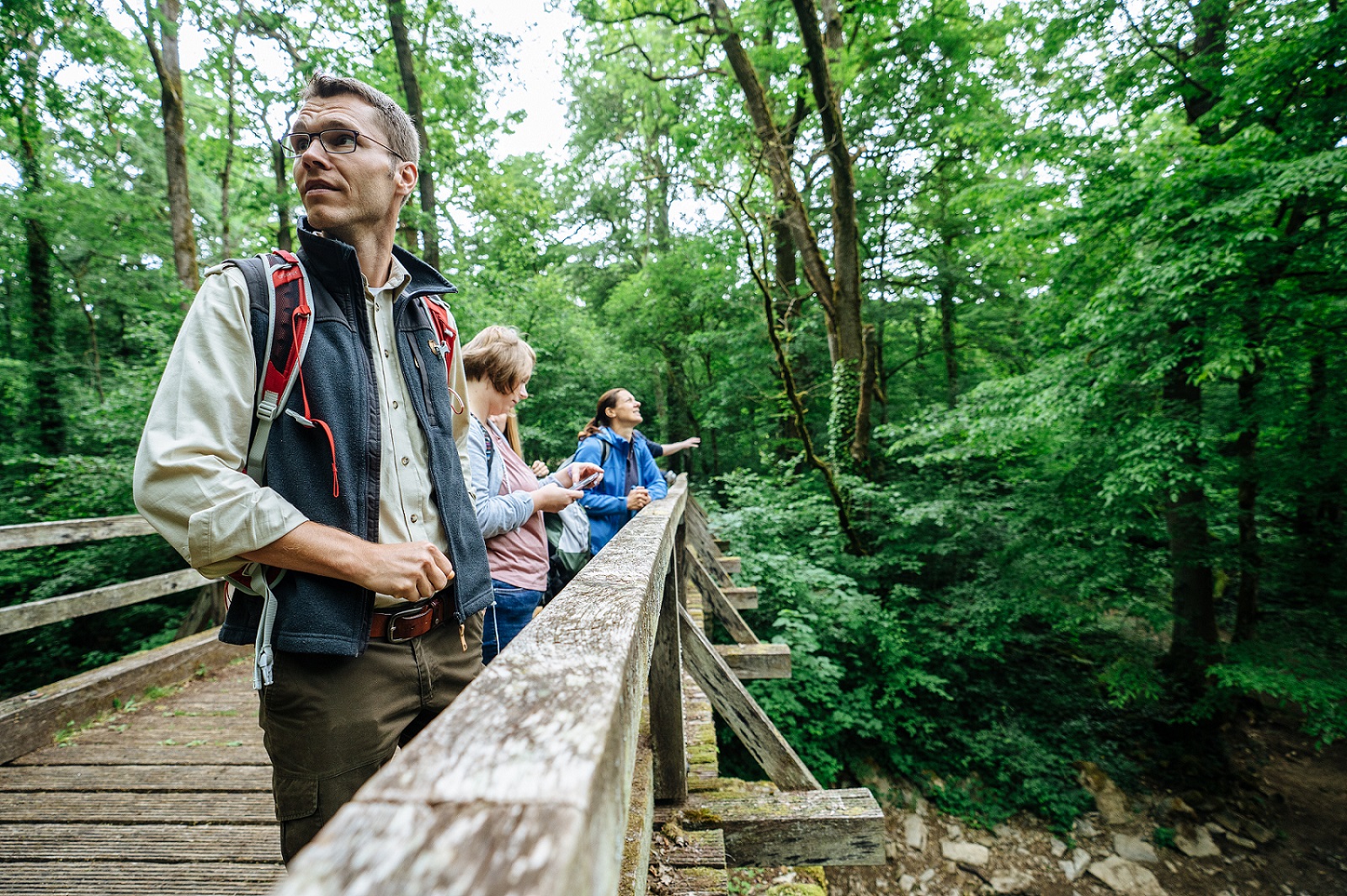 Portrait du guide de randonnée Luc Roeder. Il regarde la forêt en se tenant sur un pont.