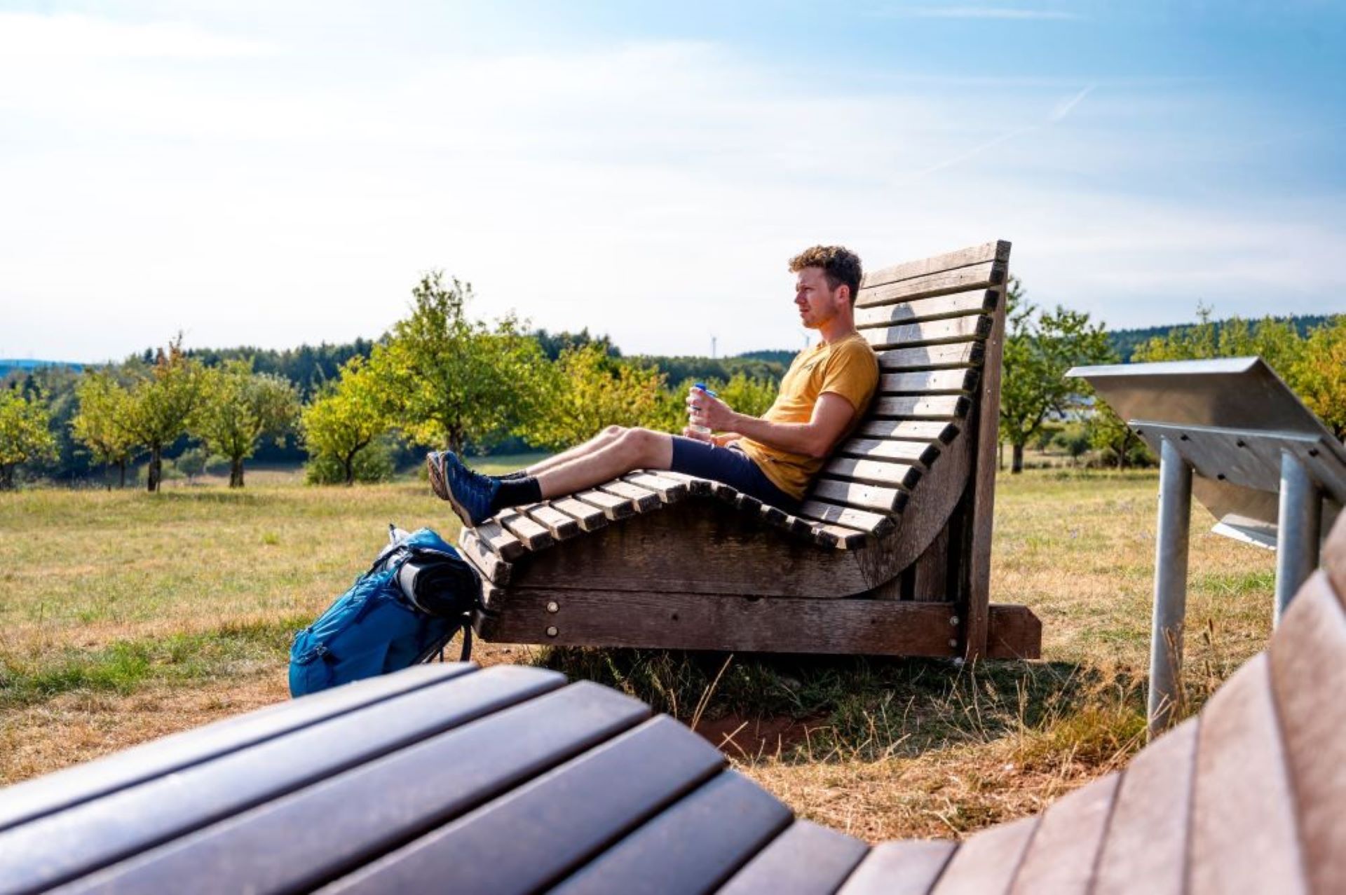 Un homme en chemise jaune est assis sur un banc de randonneur et se détend.
