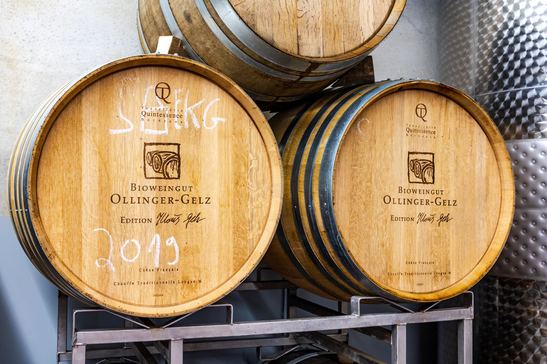 Trois barils de vin portant le nom de la cave sont empilés les uns sur les autres. Le millésime est inscrit à la craie blanche sur les barriques.