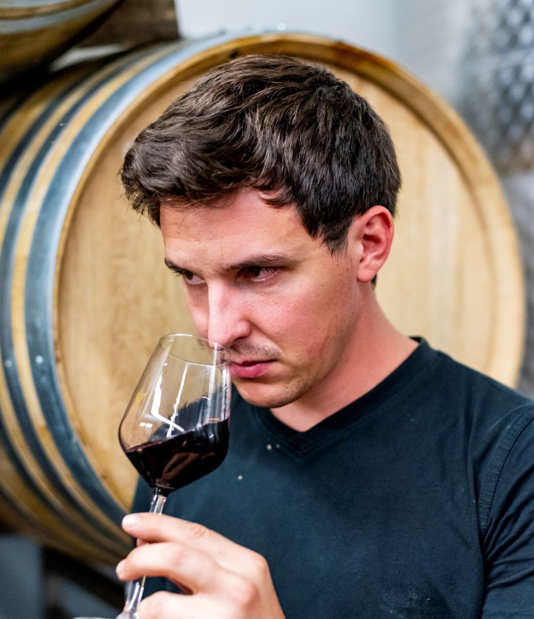 Le jeune vigneron, visage sérieux et chemise bleue, hume un verre de vin de sa cave.