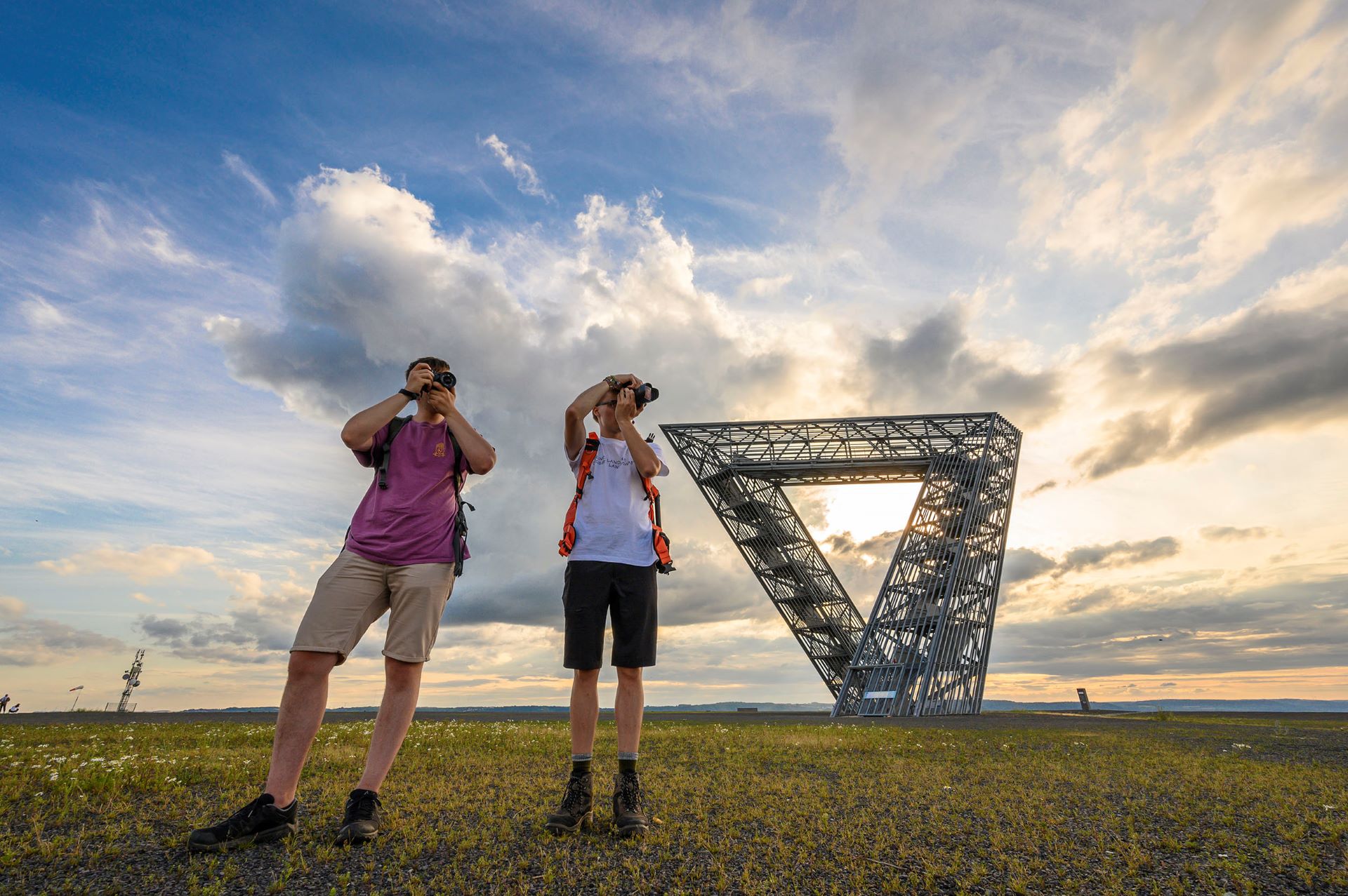 Deux membres du collectif Saarroamers photographient la vue depuis le sommet de la colline de Saarpolygon. Derrière eux, on peut voir le Saarpolygon sur fond de ciel bleu nuit avec des nuages.