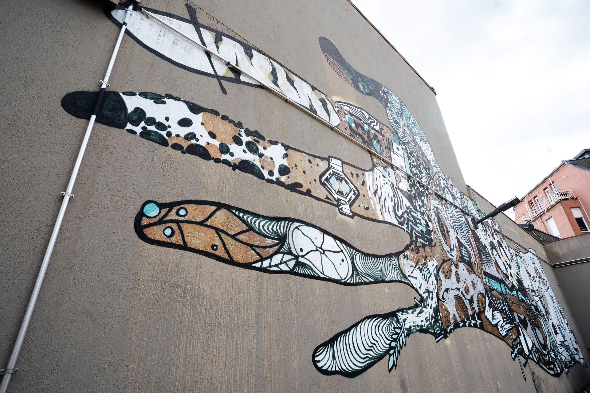 Un grand mur de béton d'un bâtiment est peint avec des graffitis : une main tendue est peinte de manière stylistique avec des blocs de couleurs et de motifs.