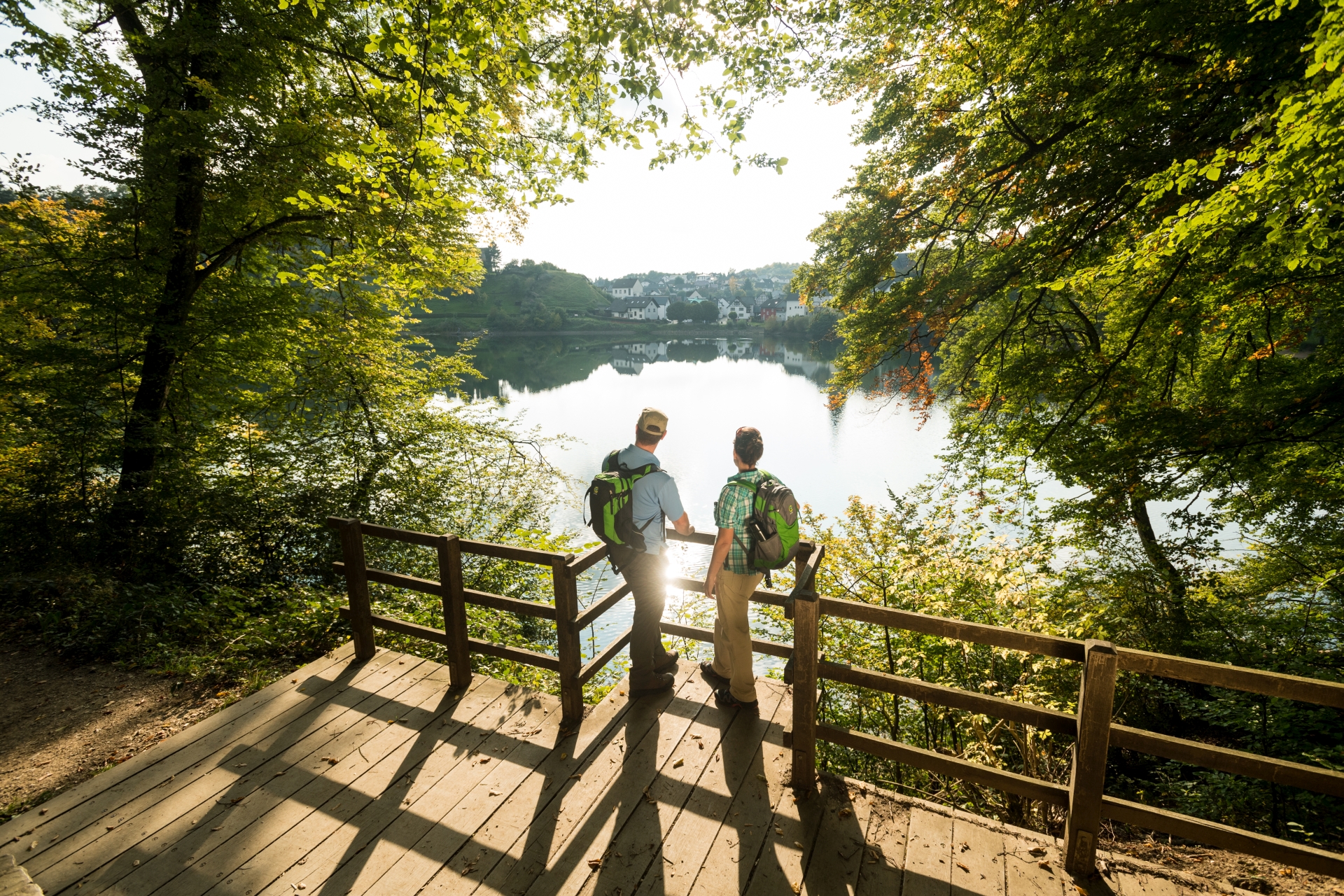 Deux personnes en tenue de randonnée se tiennent au Maar d'Ulmen et regardent l'eau.