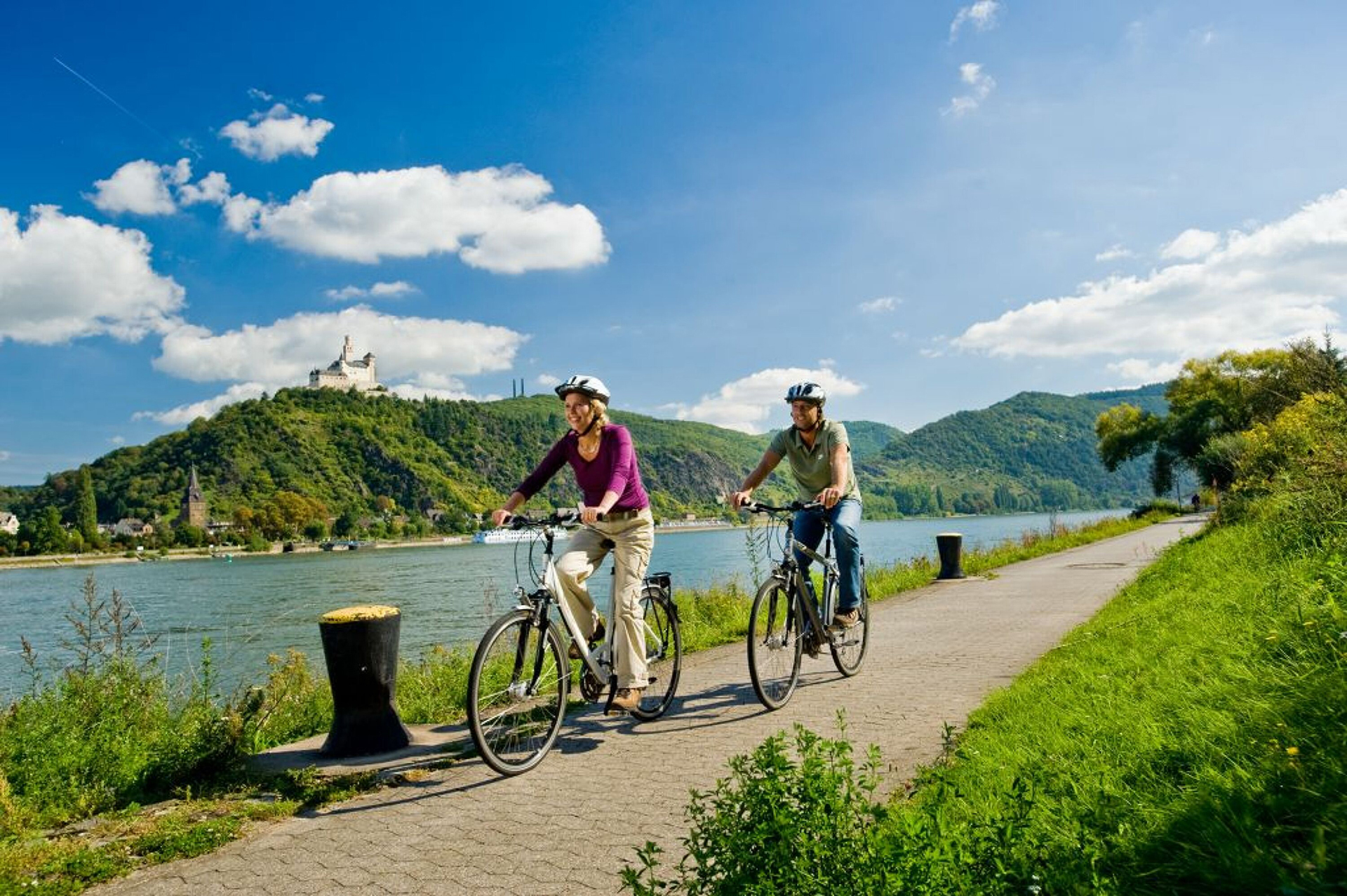 Un couple à vélo sur la piste cyclable du Rhin près de la petite ville de Brey avec une belle vue sur le château de Marksburg.