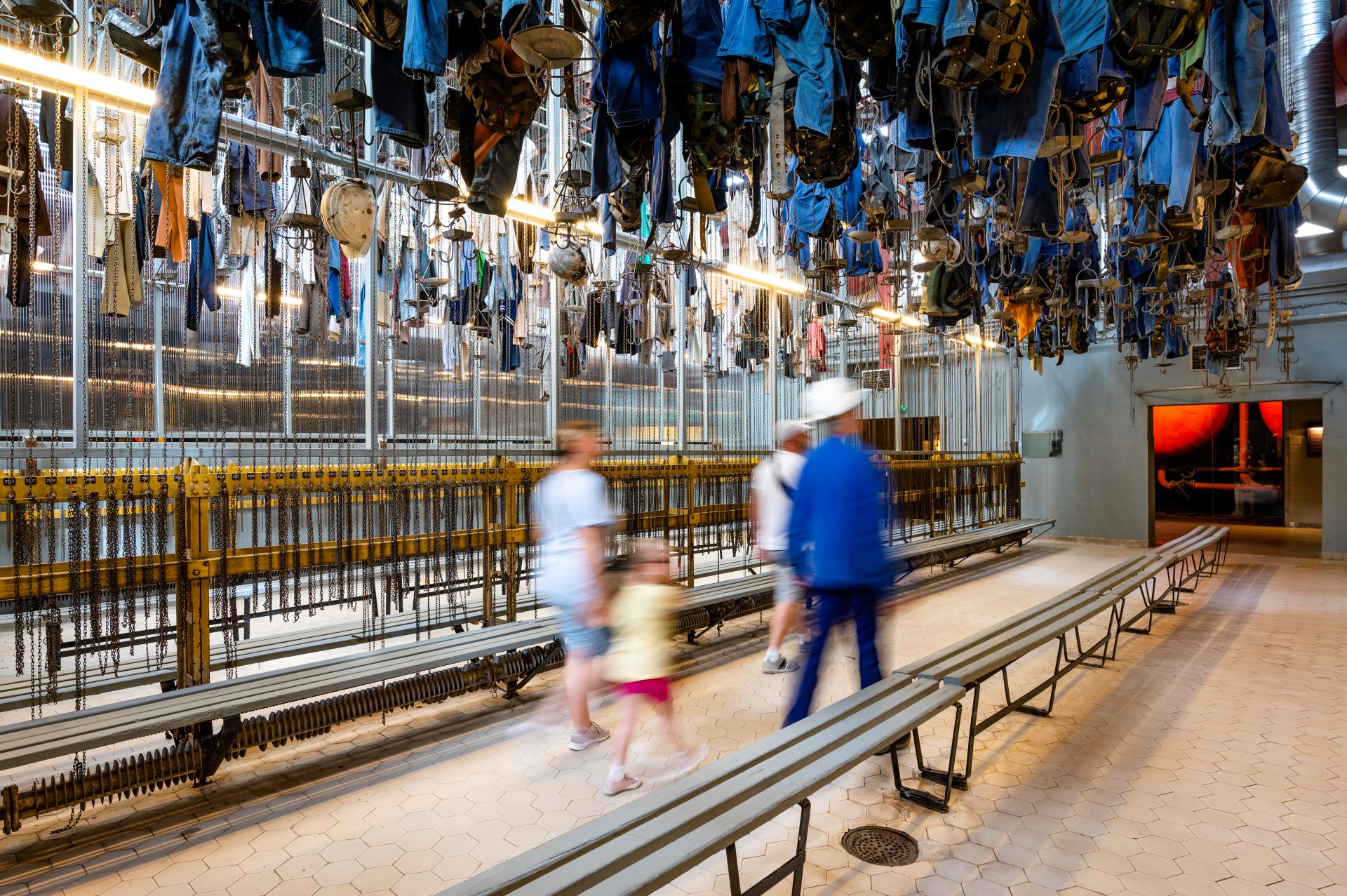 La famille et le guide touristique traversent une pièce de l'ancienne mine où des vêtements de mineurs sont suspendus au plafond comme pièces à conviction.