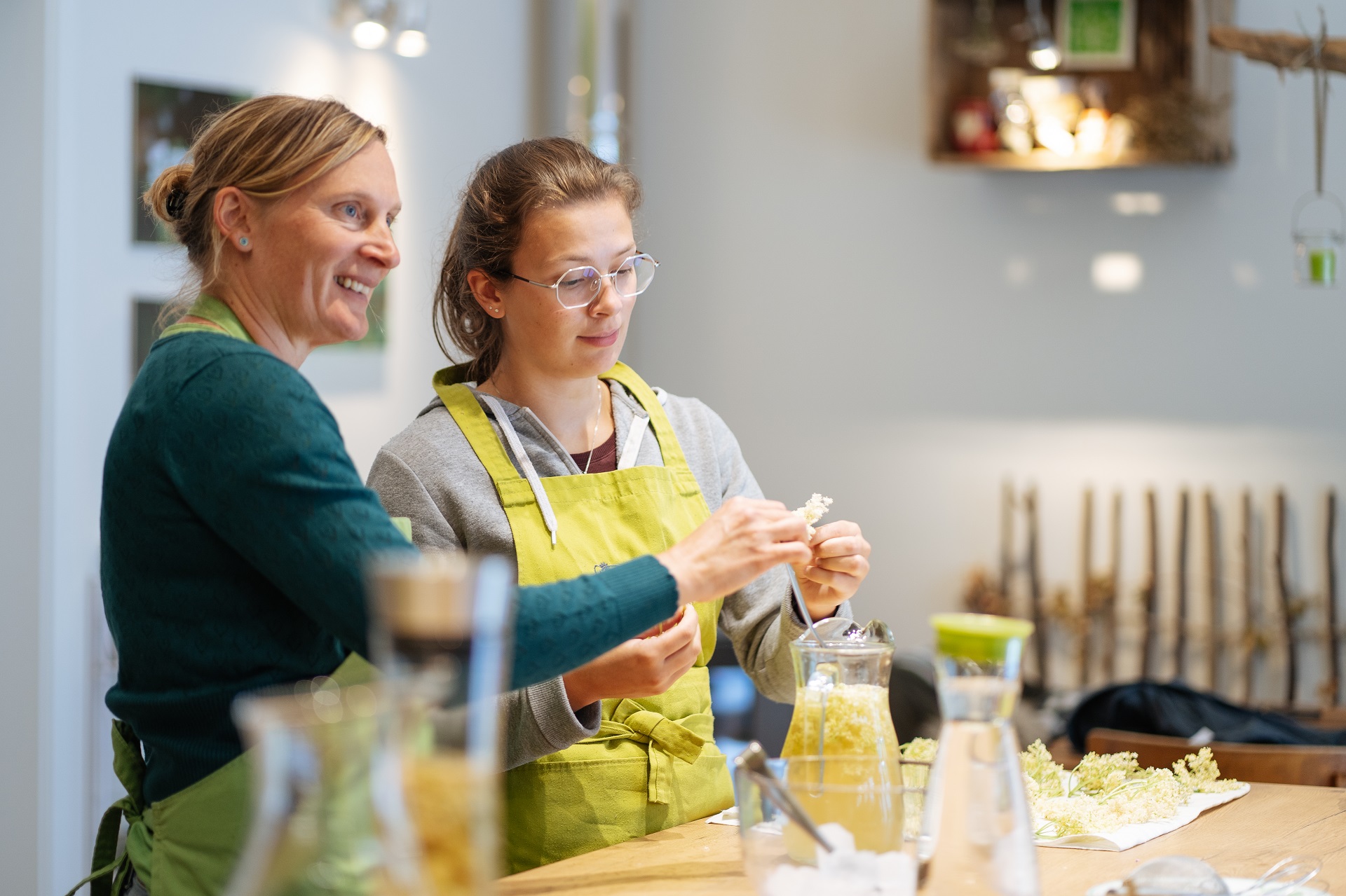 Karin Laschet und eine junge Frau zusammn in der Küche beim Weiterverarbeiten der Kräuter. Beide sind am Lächeln.