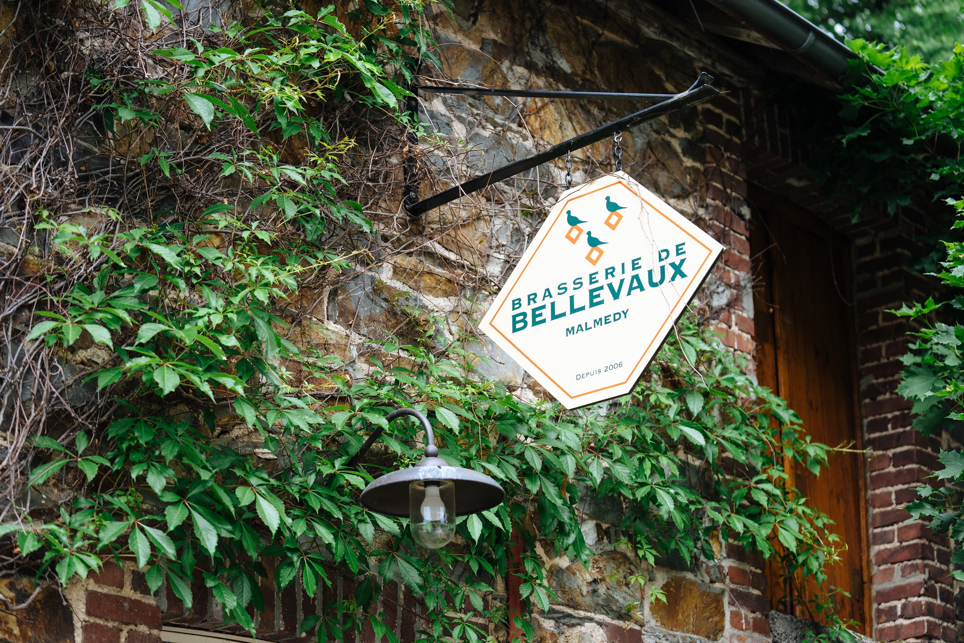 Wilder Wein rankt an der Naturstein-Fassade der ehemaligen Scheune empor. An der Hausfassade ist ein Bild mit der Aufschrift "Brasserie de Bellevaux" angebracht.