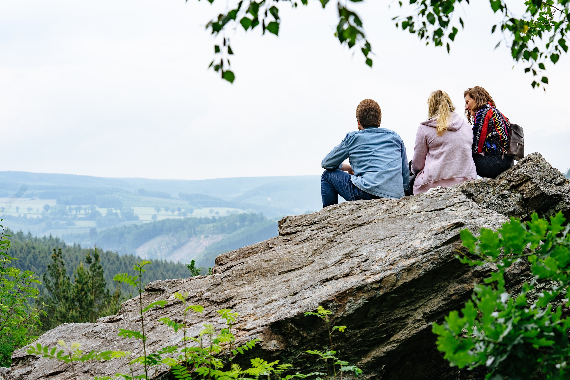 Drei junge Leute sitzen auf einem Felsvorsprung und schauen in das Tal Bellevaux.