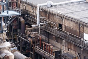 Ein Teil des Industriekomplexes ist von oben zu sehen. Viele Rohre und verschiedene Gebäudeelemente sind sichtbar.