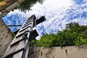 Der Panorama-Lift von Luxemburg von unten gen Himmel fotografiert. Der Himmel ist blau mit weißen Wolken. Der Lift ist umgeben von hohen Häuserfassaden.