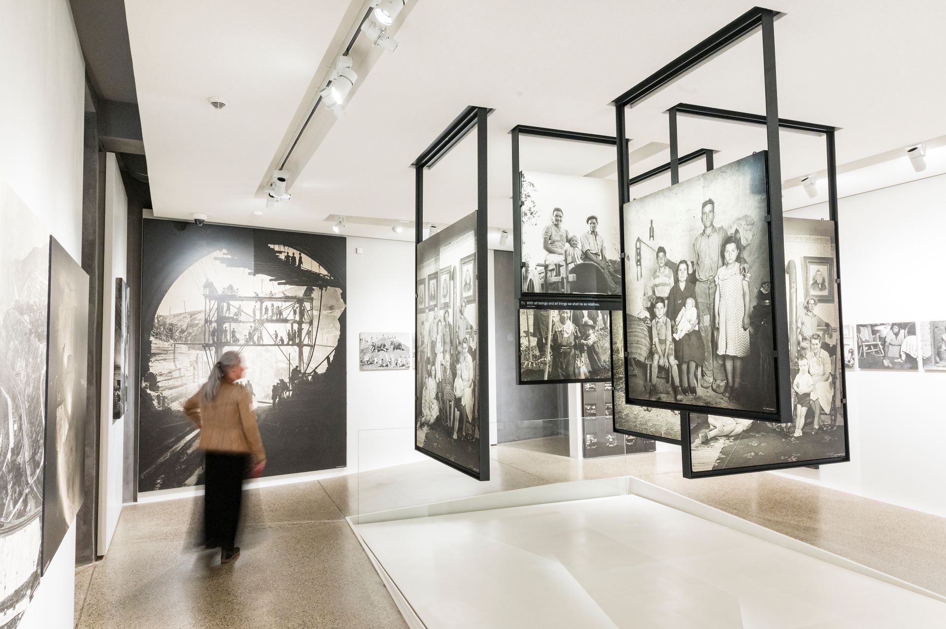 In einer Galerie hängen schwarz-weiße Bilder von der Decke. Eine Frau geht durch die Ausstellung.