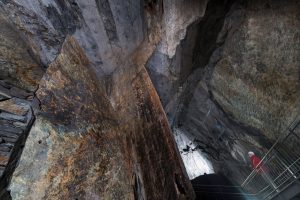 Tief im Inneren der Mine betrachtet ein Museumsbesucher mit Helm die rostfarbenen Felsformationen.