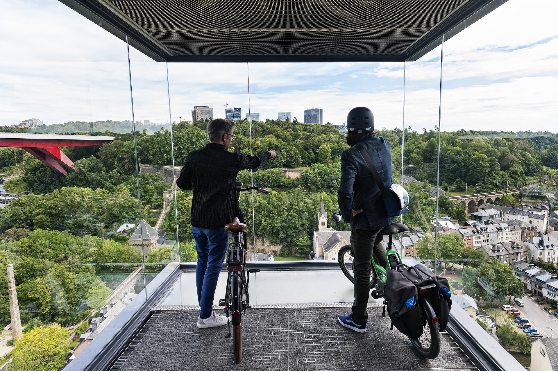 Zwei Radfahrer, die am Aussichtspunkt des Liftes stehen und auf die Stadt herunterblicken.