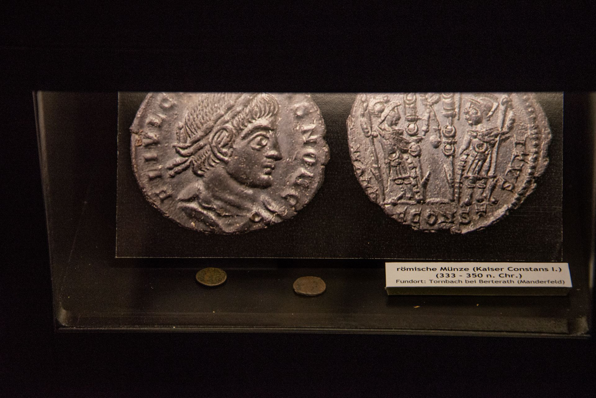 Zwei antike römische Münzen, die in einem Museum ausgestellt sind, sind vor einem dunklen Hintergrund scharf gestellt.