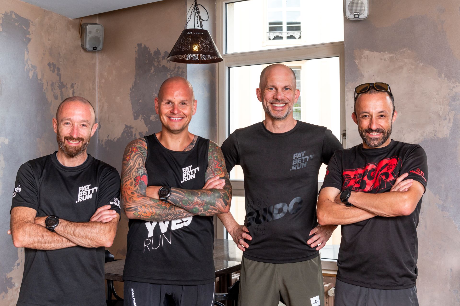 Die vier männlichen Gründer von FatBetty.run sind auf diesem Foto abgebildet und tragen schwarze Shirts mit dem Logo des Laufteams. Die Gründer lächeln und schauen direkt in die Kamera.