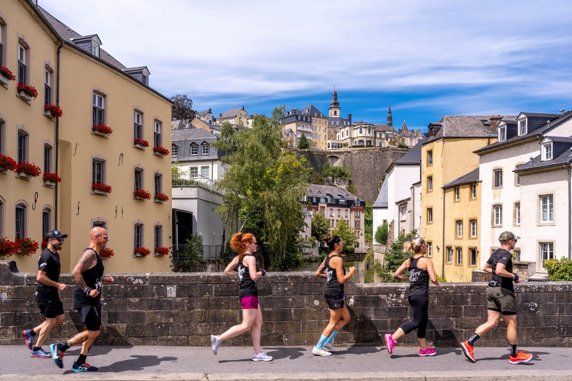 Eine Action-Aufnahme der Läufer bei ihrem Lauf. Die Läufer sind im Vordergrund abgebildet, im Hintergrund sind Stadtansichten und die Festungsmauern von Luxemburg zu sehen.