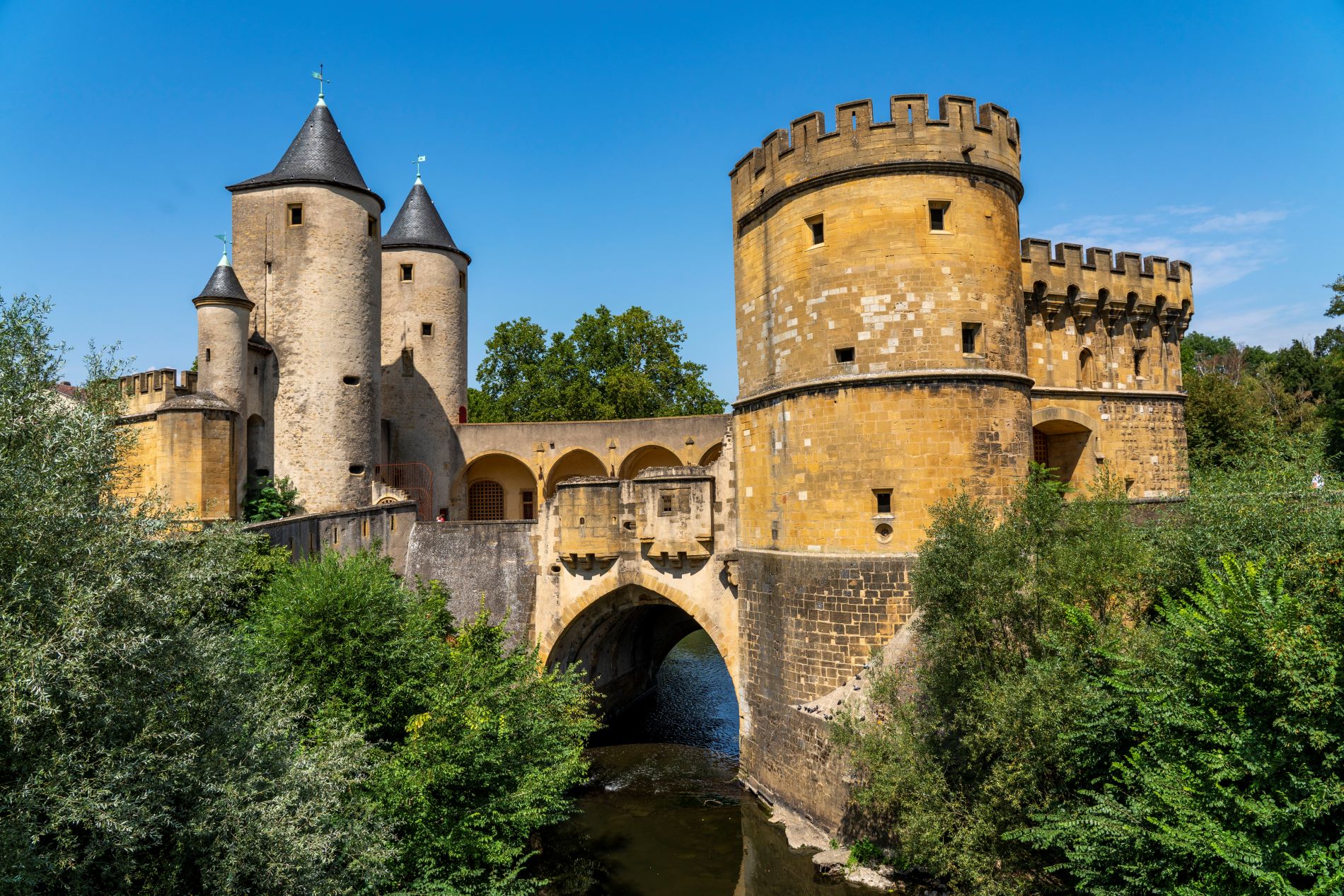 Eine alte Festung überspannt den Fluss. Sie ist aus gelben und grauen Ziegeln gebaut und hat drei Türme auf der linken Seite und große runde Türme auf der rechten Seite.