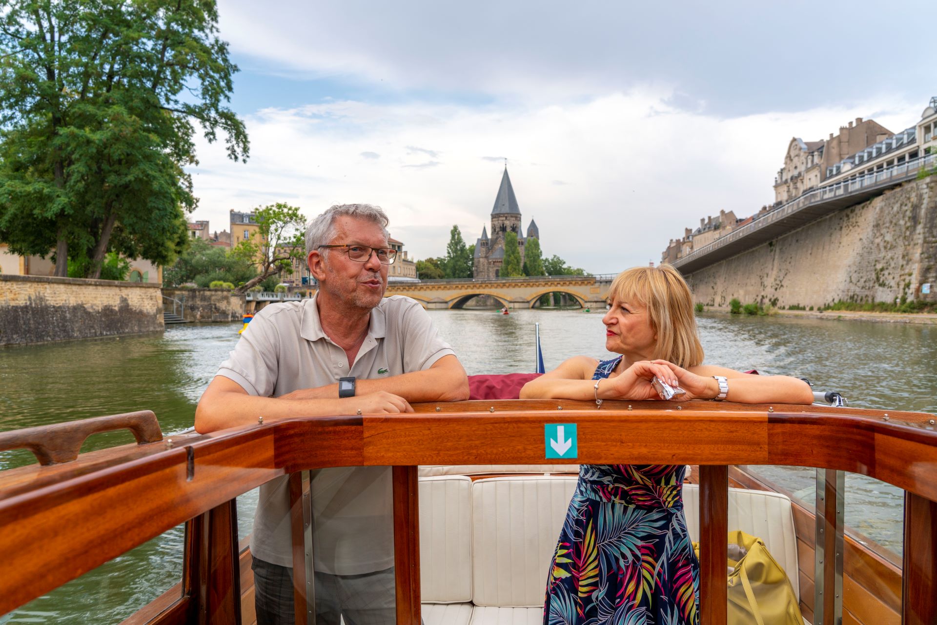 Zwei Gäste stehen hinten in einem Boot auf einem Fluss durch Metz, während sie eine geführte Tour genießen.