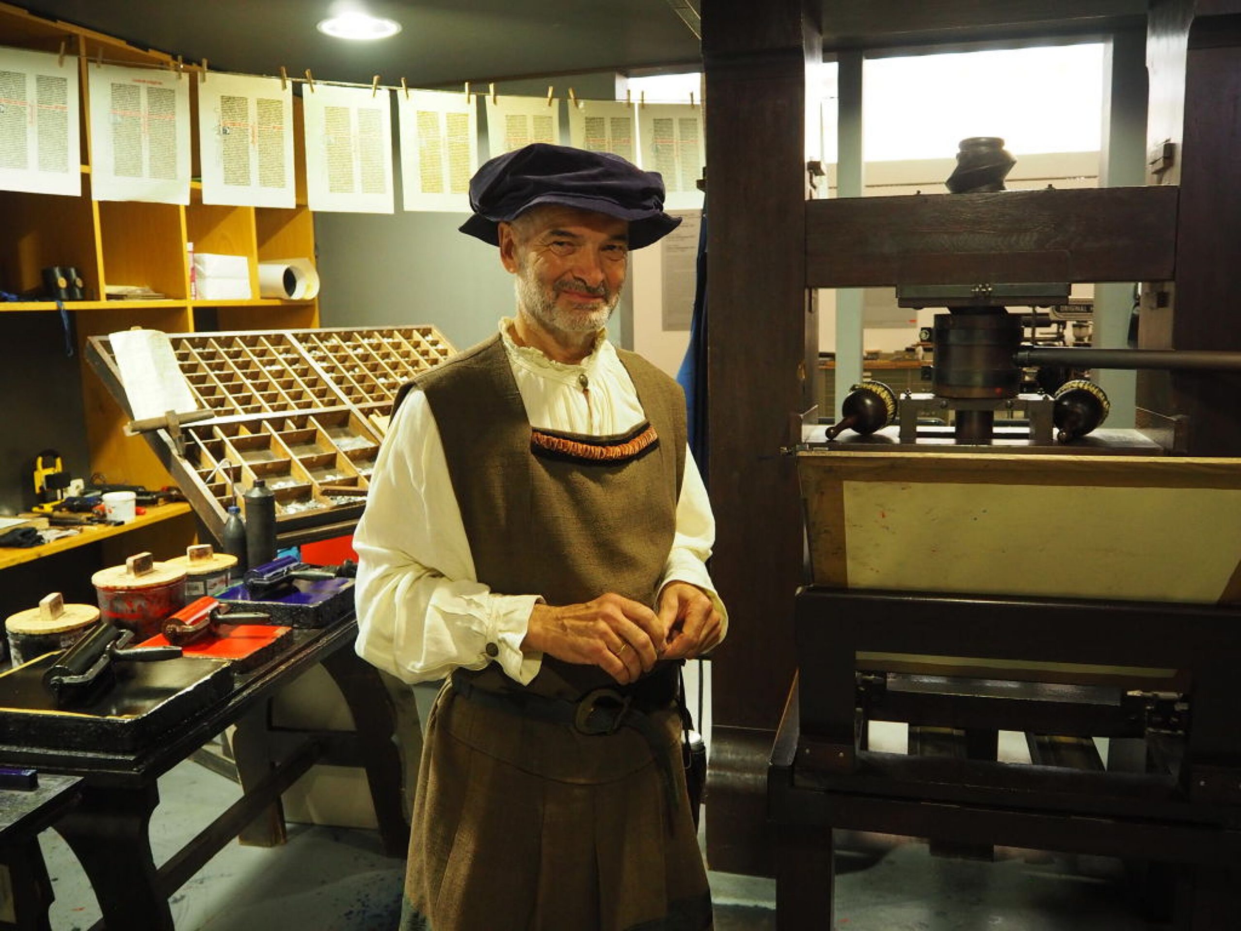 Dr. Elmar Rettinger steht, kostümiert als Johannes Gutenberg, neben einer Druckerpresse im Gutenberg-Museum