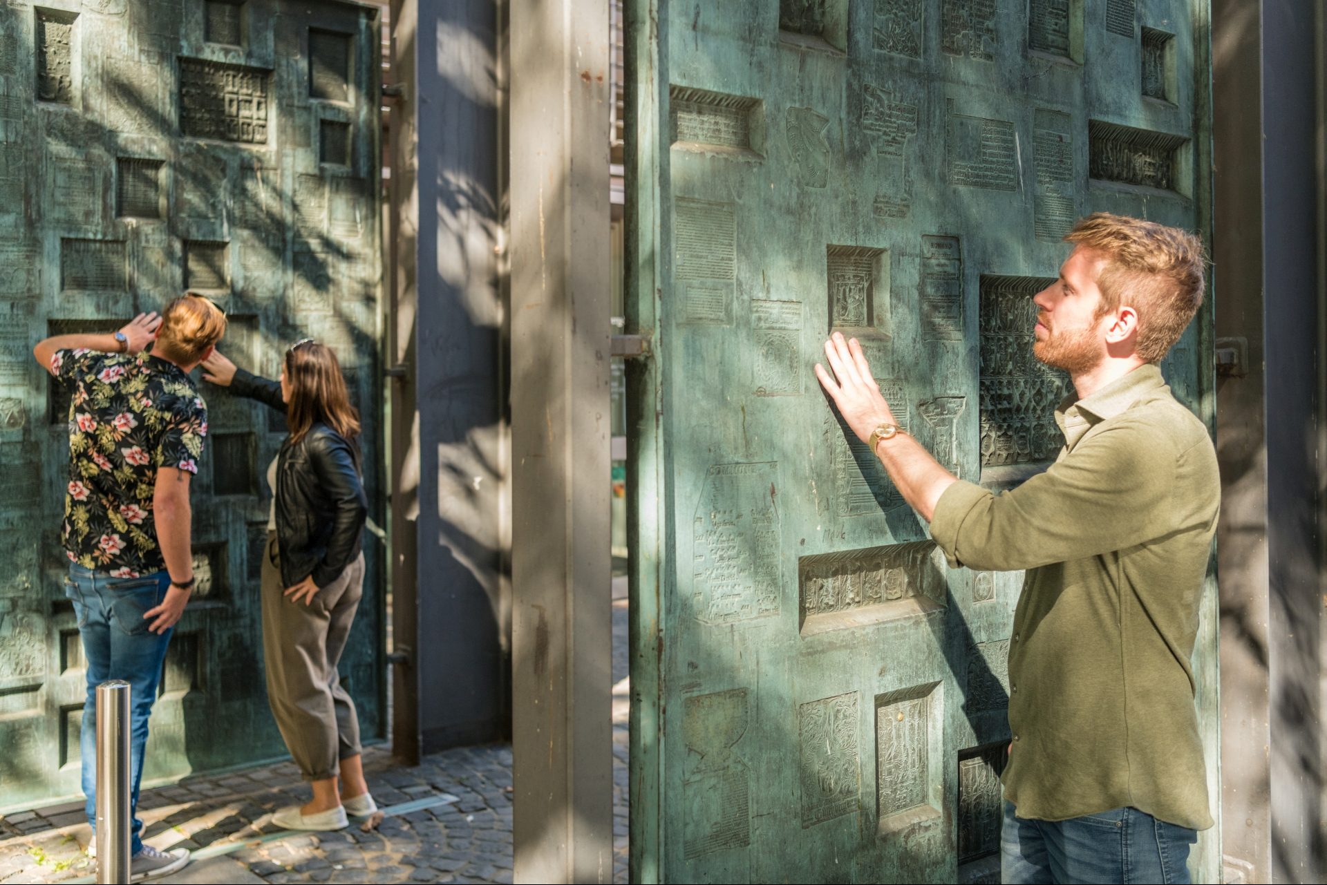 Ein junges Pärchen und ein junger Mann entdecken Exponate an der Fassade des Gutenberg-Museums