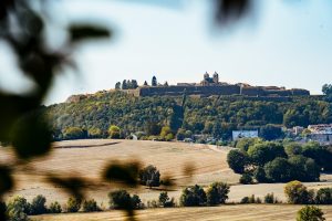 Landschaftsaufnahme. Im warmen Licht der Sommersonne sieht man in einiger Entfernung die Festungsmauern von Montmedy