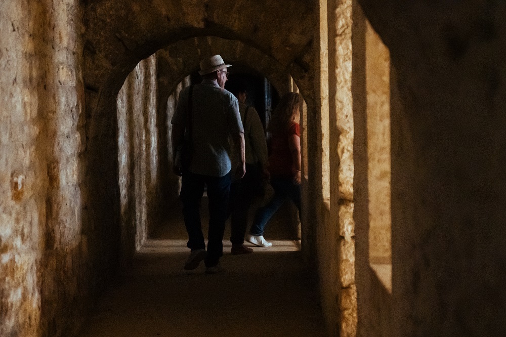 Die Besucher wandern durch einen dunklen Gang im Inneren des Festungswalls. An manchen Stellen dringt Licht ins Innere, sodass die Besucher schemenhaft zu sehen sind.